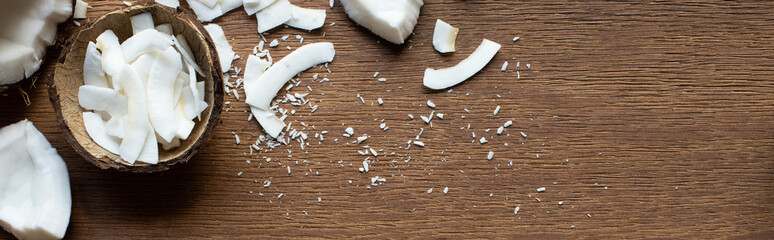 top view of fresh tasty coconut half near flakes in shell on wooden table, panoramic shot