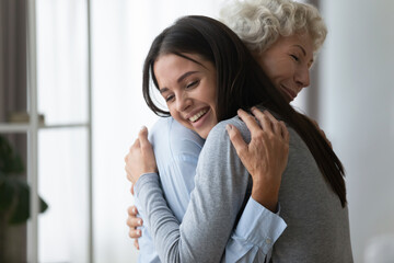 Grown up adult smiling 20s granddaughter embraces elderly grandmother glad to see missing her,...