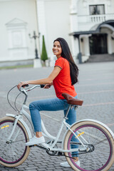 Fototapeta na wymiar Beautiful smiling girl in a red T-shirt with water in her hands stands near the bike