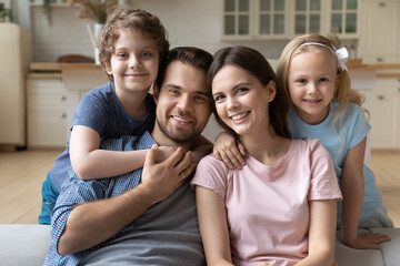 Portrait of happy young Caucasian family sit on couch in kitchen posing with little preschooler...