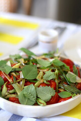 Bowl of green leaf vegetables, fried tomatoes and risoni pasta salad, sreved on a table. Selective focus.