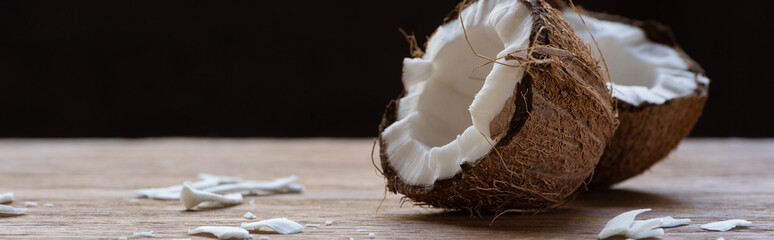 selective focus of fresh tasty coconut halves and flakes on wooden table isolated on black,...