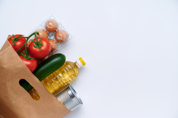 Red tomatoes, zucchini, chicken eggs, canned food, sunflower oil in paper bag. Fresh vegetables in the bag, top view flatlay photo on white background. The concept of healthy diet