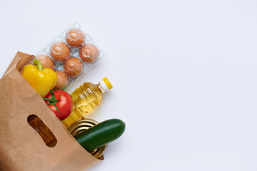 Red tomatoes, zucchini, yellow pepper, chicken eggs, canned food, sunflower oil in paper bag. Fresh vegetables in the bag, top view flatlay photo on white background. The concept of healthy diet