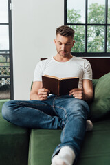 Selective focus of man reading book on couch at home