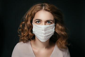 Beautiful young woman wears a respiratory mask, a beautiful female face looks at the camera, a pandemic, a woman's face on a black background