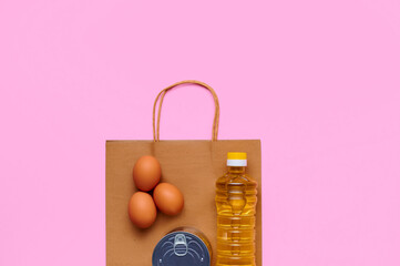 Products from the store and paper bag. Chicken eggs, sunflower oil, canned food on a pink background. Food supplies crisis food stock for quarantine isolation period