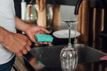 Fototapeta na wymiar Cropped view of man holding sponge near wet wine glass and kitchen sink