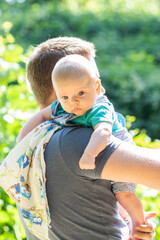 Cute little baby boy spending weekend time with his dad outside. Baby burps on father's shoulder in green park scenery - vacation summer time with baby.