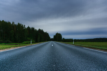 Fototapeta premium Suburban highway without cars in cloudy day. Stormy weather on county road.