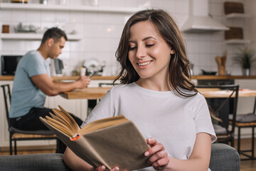 selective focus of cheerful woman reading book near mixed race man at home