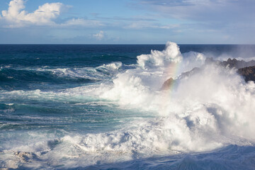 Large surf wave with rainbow in spray is crashing over a volcanic shore on Tenerife island, Canary Islands, Spain