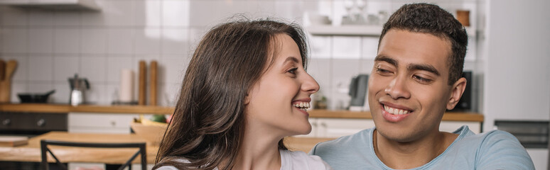 horizontal image of happy woman looking at mixed race boyfriend at home