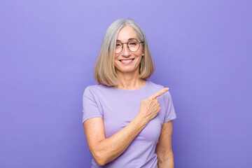 senior or middle age pretty woman smiling cheerfully, feeling happy and pointing to the side and upwards, showing object in copy space - obrazy, fototapety, plakaty