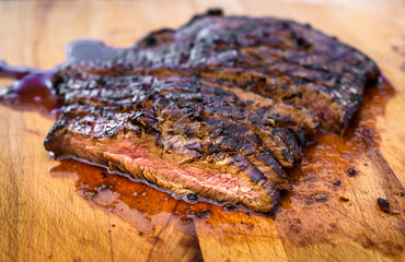 Sliced grilled juicy marinated angus beef flank steak on wooden board.