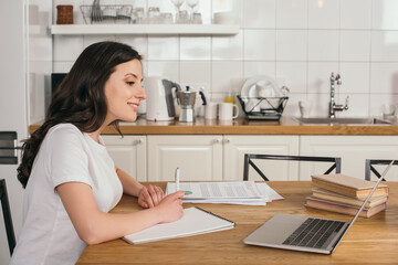 cheerful freelancer looking at laptop and writing in notebook, online study concept