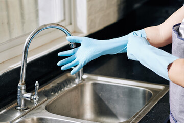 Hands of housewife putting on rubber gloves before cleaning surfaces in kitchen