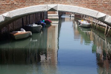 Fototapeta na wymiar Anchored boats under a bridge in venice in Arsenal disctrict, Italy