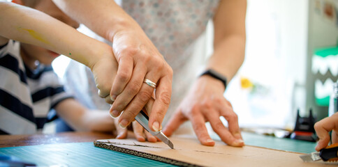 Mother helping son to cut cardboard, quarantine project	
