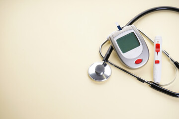 Digital glucometer, lancet pen and stethoscope on a yellow background with space for text. Diabetes concept, blood glucose meter.