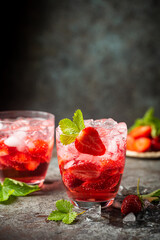 Refreshing summer drink with strawberry slices in glasses on dark background