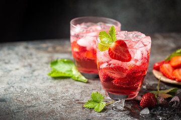 Refreshing summer drink with strawberry slices in glasses on dark background