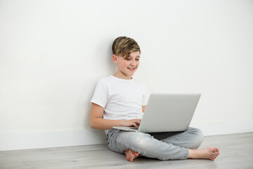 Smiling boy chatting with friends in social networks sitting front laptop .Online study, education .Young boy learning at home during quarantine