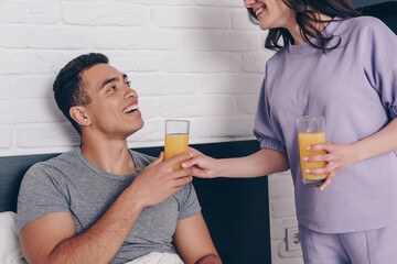 cheerful woman giving glass of orange juice to mixed race boyfriend in bedroom