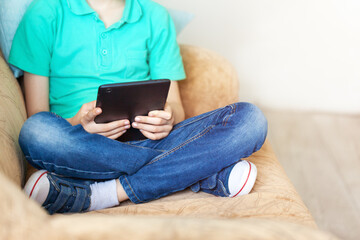 Child boy using digital tablet and headphones on sofa in living room.
