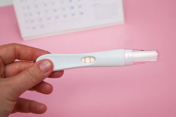 Person holding a positive Pregnancy test with calendar behind and pink background. Being pregnant concept. Healthcare concept. Pregnancy concept. 