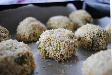 Vegan Green Bean Balls rolled in sesame seeds, placed in a metal pan, ready to bake. Close up view.