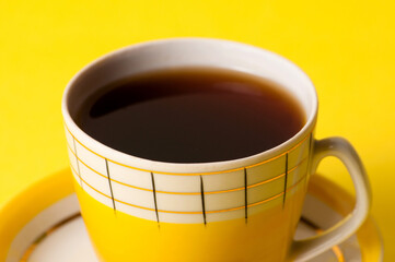 Yellow cup of tea or coffee without foam, close-up on a yellow background. Minimalistic composition with vintage subject and place for text.