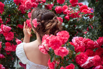 Portrait of pretty bride dressed wedding white dress, make up and hairstyle posing at the background  flowers roses wall at the morning with wind in hair.