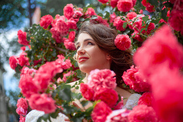 Fototapeta premium Portrait of pretty bride dressed wedding white dress, make up and hairstyle posing at the background flowers roses wall at the morning with wind in hair.