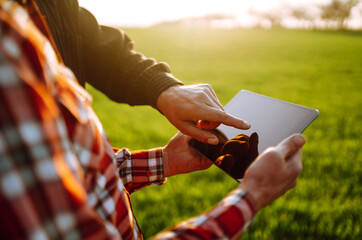 Farmers reading and discussing a report in a tablet computer on an agriculture field at sunset....