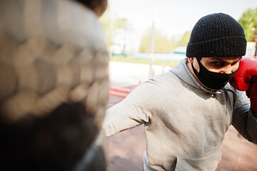 Fototapeta premium Portrait sports arabian boxer man in black medical face mask boxing outdoor during coronavirus quarantine.