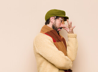 young cool bearded man feeling disgusted, holding nose to avoid smelling a foul and unpleasant...