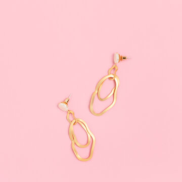 Golden earrings on a pink pastel background. Woman accessories layout.