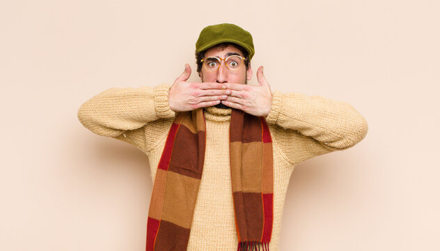 young cool bearded man covering mouth with hands with a shocked, surprised expression, keeping a secret or saying oops