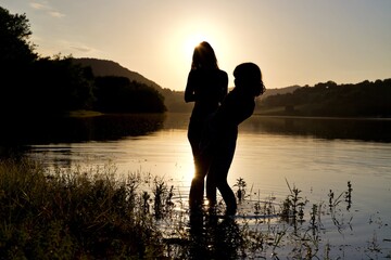 Silhouettes mère et fille au coucher de soleil - portrait femme couple duo ombre - lac plage...