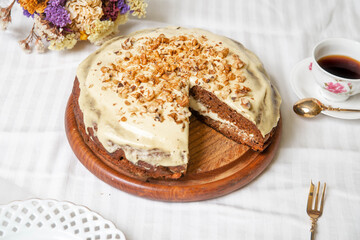 Carrot cake with nuts, on the white textile material, with flowers and a cup of coffee.