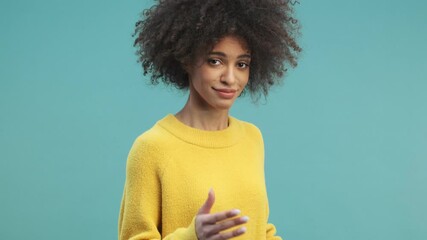 An attractive young african american woman with curly hair is moving like a robot isolated over blue wall background in studio