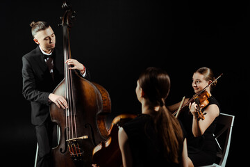 Fototapeta premium trio of musicians playing on double bass and violins isolated on black