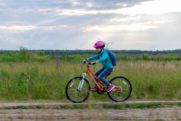 Fototapeta na wymiar A little girl rides a bicycle on a country road along the meadow.