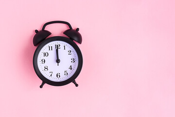 View from above on black alarm clock on pink background. 12 a.m. Time is now
