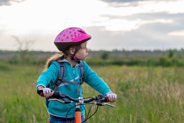 A child in a bicycle helmet stands with a bicycle in the meadow.