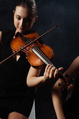 professional beautiful musicians playing classical music on violins on dark stage