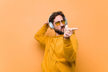 young crazy cool man listening music with headphones against orange wall