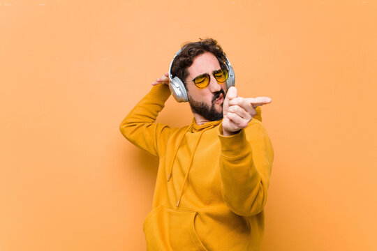 young crazy cool man listening music with headphones against orange wall