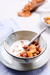 Healthy breakfast yogurt bowl with granola and caramelized bananas and nuts on grey concrete background. Selective focus